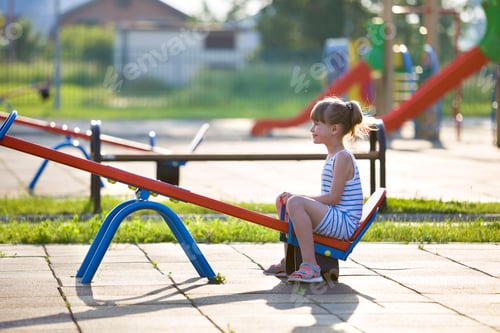 Preview: Cute young child girl outdoors on see-saw swing on sunny summer day.