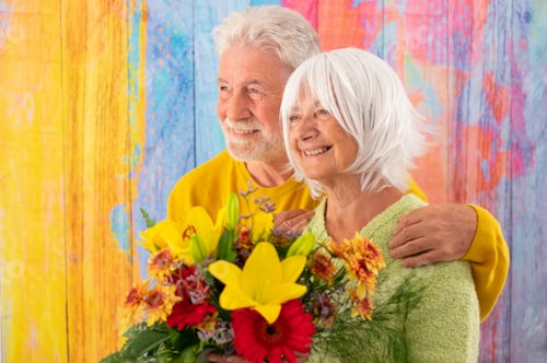 Preview: Attractive pleased elderly woman receives flowers as present for anniversary of Valentine day