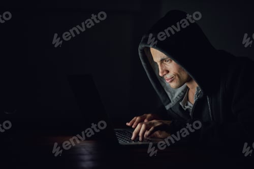 Preview: Protect yourself before its too late. Shot of a hooded computer hacker using a laptop in the dark.