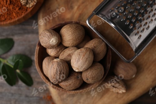 Preview: Nutmegs in bowl and grater on wooden table, flat lay