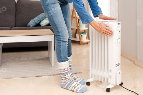 Preview: Person with winter socks warming hands on a Radiator in a living room, Energy Efficiency concept