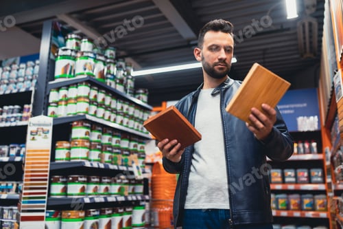 Preview: a man in a building hypermarket in the paint and varnish department chooses varnish and paint for