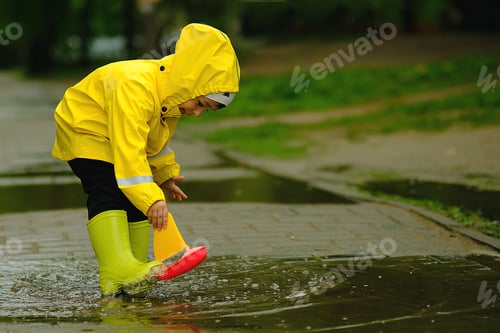 Preview: Cute child playing in a puddle with a ship on a summer rainy day.