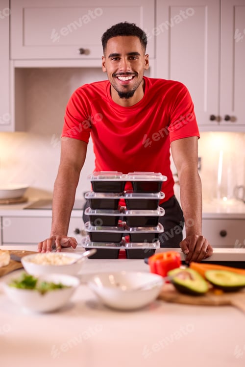 Preview: Portrait Of Man In Kitchen Wearing Fitness Clothing Making Batch Of Healthy Meals For Freezer
