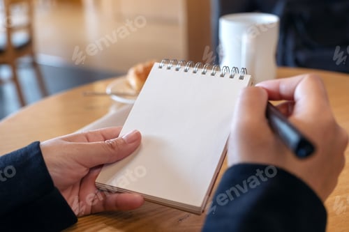 Preview: a woman holding and writing on blank notebook with croissant in a plate on table in cafe
