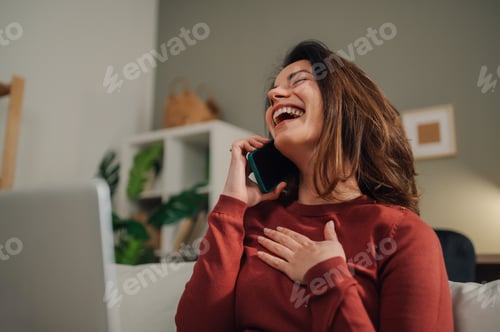 Preview: Happy woman laughing while talking on mobile phone at home