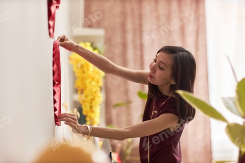 Preview: Young Adult Asian Woman Decorating Wall with Festive Ornaments during Holiday
