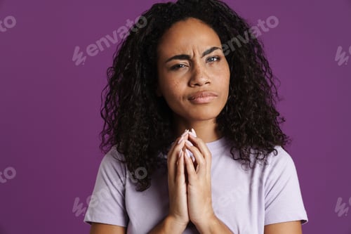 Preview: Young black woman wearing t-shirt frowning while holding hands together