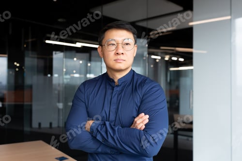 Preview: Asian serious and thinking man inside office looking out the window, businessman with crossed arms