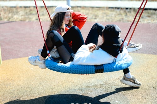 Preview: two teenager girls in caps on the playground. children's swing.