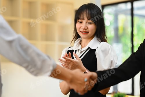 Preview: Smiling young female employee clapping hands while businesspeople shaking hands.