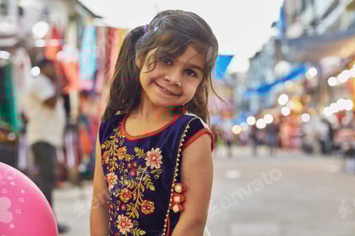 Preview: Little girl smiling on a bustling street with balloon in hand.