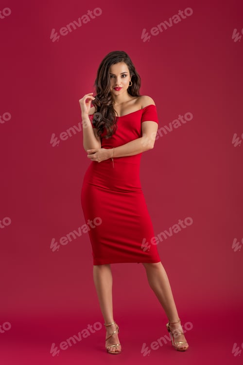 Preview: sexy girl in elegant dress and high heeled sandals looking at camera while posing on red background