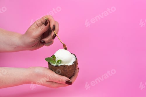 Preview: Vanilla ice cream balls in a fresh coconut half, decorated with mint leaves in the hand with a spoon