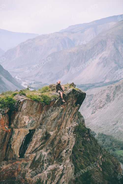 Preview: man sitting on cliff and looking at majestic mountains in Altai, Russia