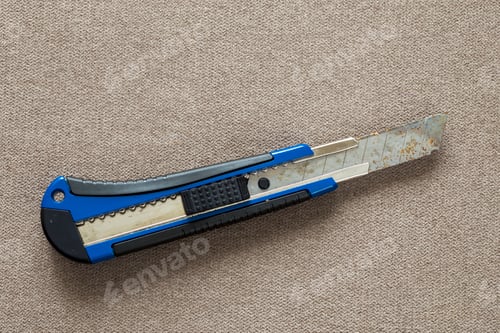 Preview: Close-up of isolated stationery retractable metallic knife with sharp blade on light cloth copy