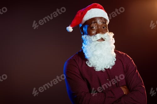 Preview: cheerful african american man in santa hat and beard posing with crossed arms on black with backlit
