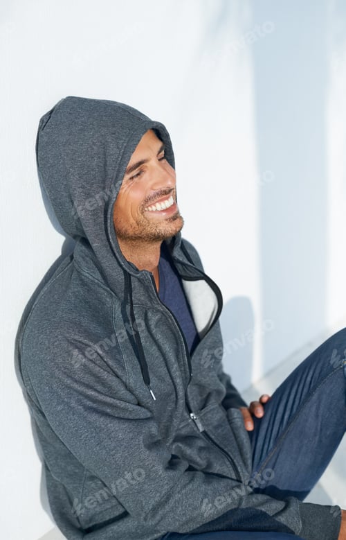 Preview: Happy to hangout. A handsome young man sitting on the floor and smiling while wearing a hoodie.