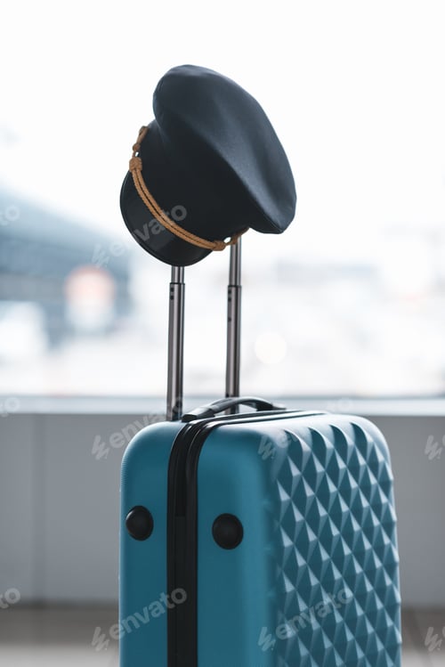 Preview: pilot cap hanging on handle of suitcase at airport