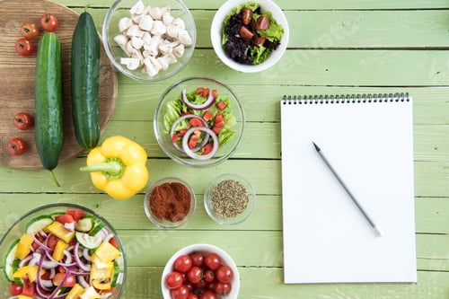 Preview: Top view of fresh raw vegetables and salads in bowls and blank notebook with pencil on wooden table