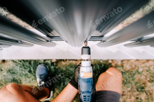 Preview: Construction worker using screwdriver and drilling screws into metal fence