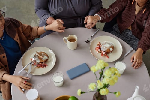 Preview: Top View Black Family Sitting at Dining Table Holding Hands in Prayer