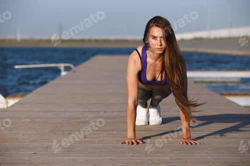 Preview: Beautiful young girl with long hair dressed in sports clothes is doing push ups on the wooden pier