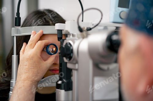 Preview: close up in an ophthalmology clinic old doctor diagnoses a young girl with a magnifying lens