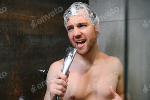 Preview: Attractive young cheerful man singing while washing in the shower, wearing shower cap