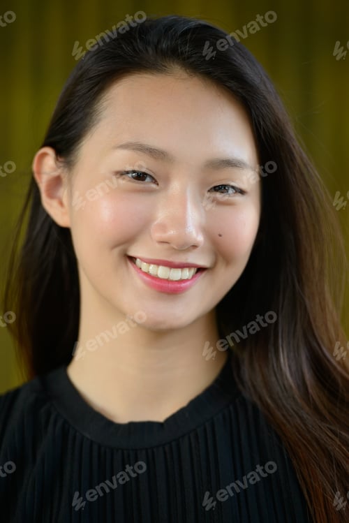 Preview: Happy young beautiful Asian businesswoman against bamboo fence
