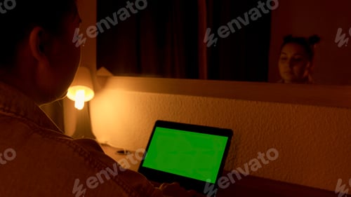 Preview: Woman sitting at the desk using laptop with green screen at night working over hours at home office