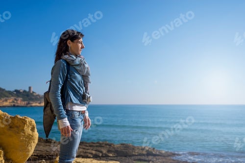 Preview: daydreaming woman wearing casual clothes standing on seashore while looking away to the horizon