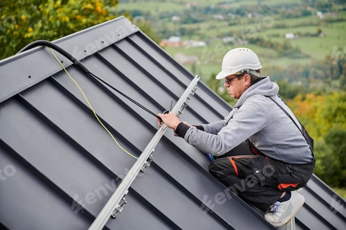 Preview: Man worker prepearing for mounting photovoltaic solar modules on roof of house.