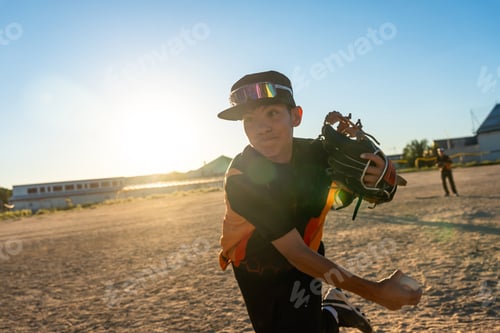 Preview: Young boy pitching baseball on a dusty field at sunset