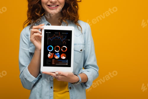 Preview: cropped view of happy curly girl holding digital tablet with charts and graphs on screen isolated on