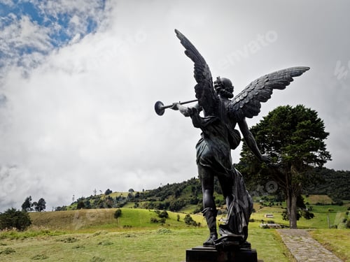 Preview: Monumental angel sculpture with a trumpet against a lush green backdrop