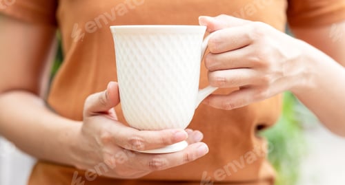 Preview: Closeup of female hands with a mug of beverage. Beautiful girl in grey sweater holding cup of tea or