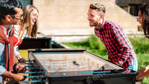 Preview: Multicultural friends play kicker table foosball at open space bar