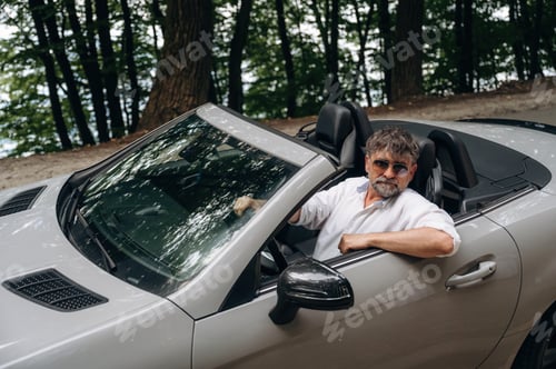 Preview: Beautiful, in sunglasses, looking at the camera. Stylish senior man is in convertible cabriolet car