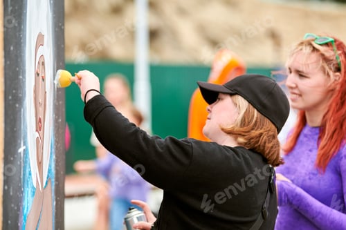 Preview: Two female artists painting picture with paint spray can spraying onto canvas at street exhibition