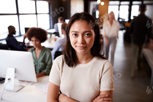Preview: Millennial Asian female creative standing in a busy casual office, smiling to camera