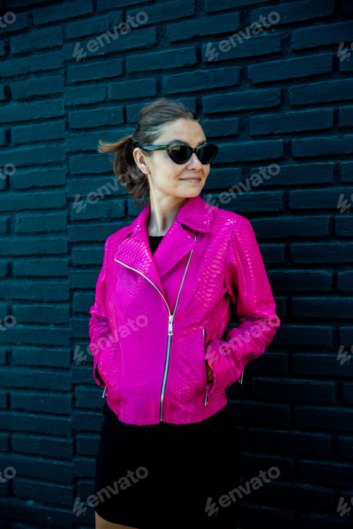 Preview: Beautiful woman in bright electric pink jacket and sunglasses on black background. Fashion concept