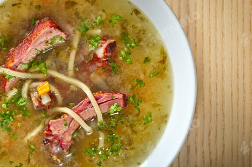 Preview: Soup of smoked ribs with vegetables and herbs in a white bowl