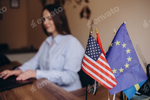 Preview: table with two flag usa and eu. A woman is working in the background