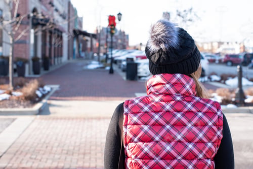 Preview: Back view of woman in vest and winter hat walking down city sidewalk