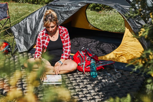 Preview: Woman planning next trip while sitting with map in tent. Woman relaxing in tent at camping