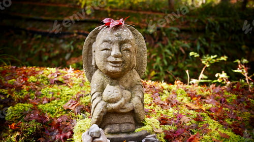 Preview: Closeup of a stone statue of a smiling Jizo Bosatsu holding a cat in the park