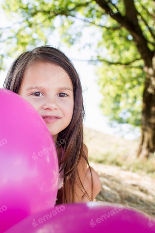 Preview: Portrait of girl hiding behind pink balloons in park