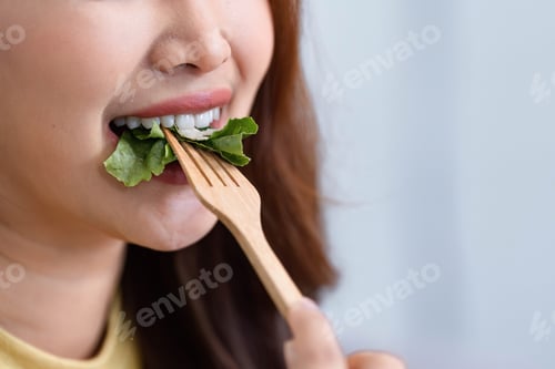 Preview: Healthy Eating and Close-Up Cooking. A woman taking a bite of fresh greens with a wooden fork.