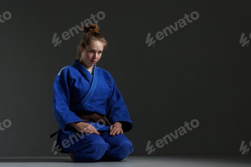 Preview: girl judoka in a white kimano with a black belt on a blue background, studio photo